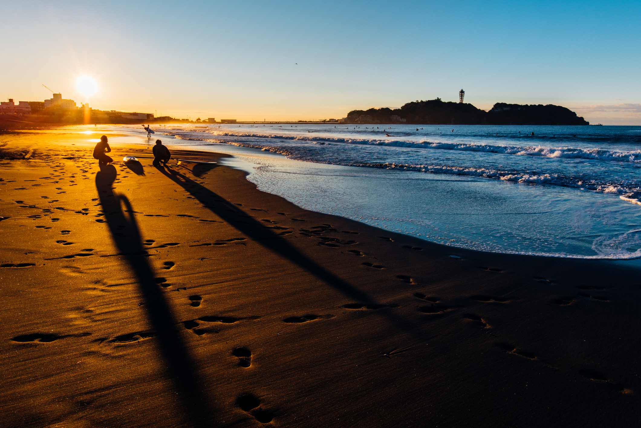 砂浜には2人の人影があり、波打ち際に近づきながら、夕日が沈む様子を見つめています。
