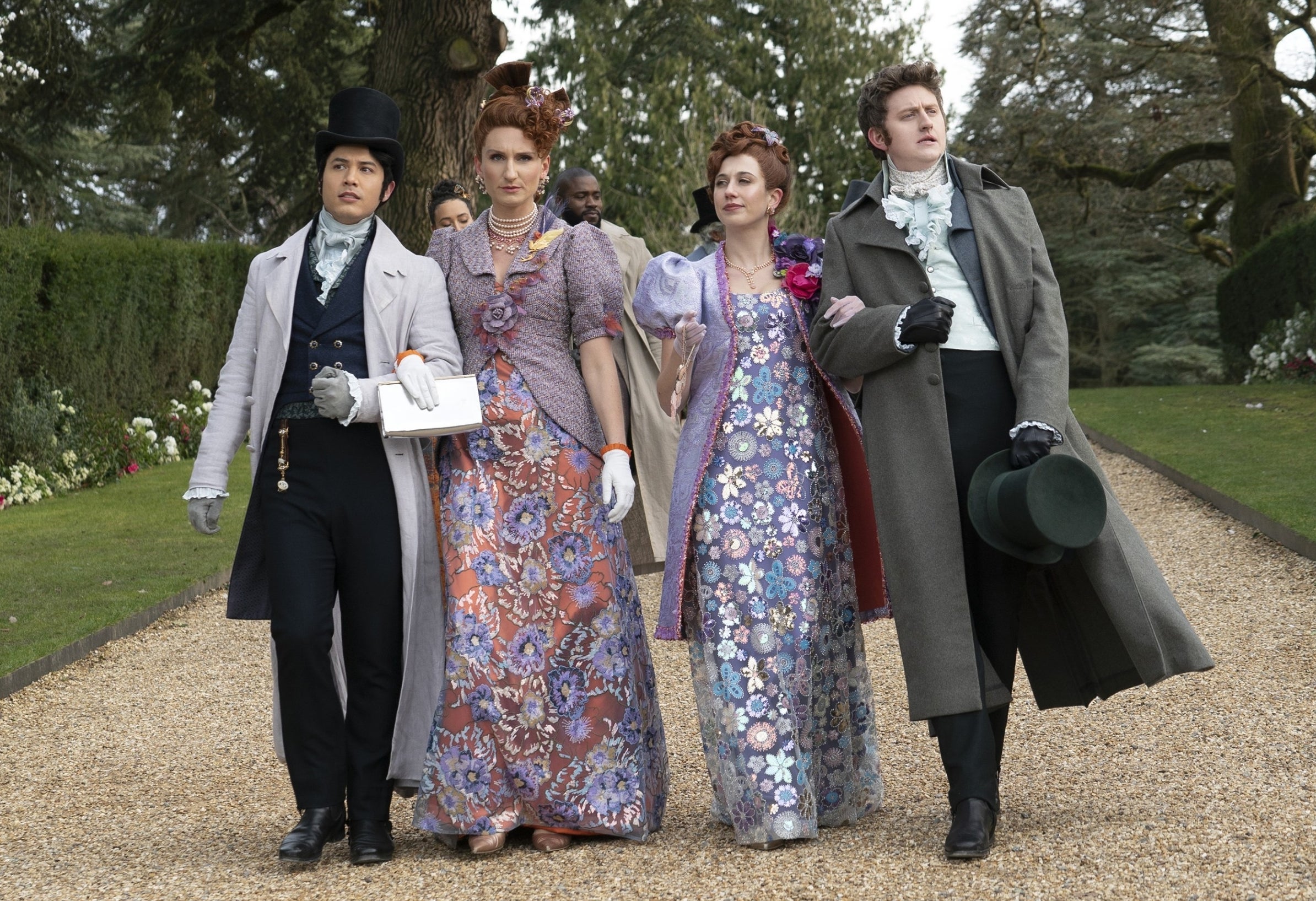 From left to right, James Phoon, Bessie Carter, Harriet Cains, and Norm Macdonald in period costume walking on a gravel path, likely in a scene from "Bridgerton."