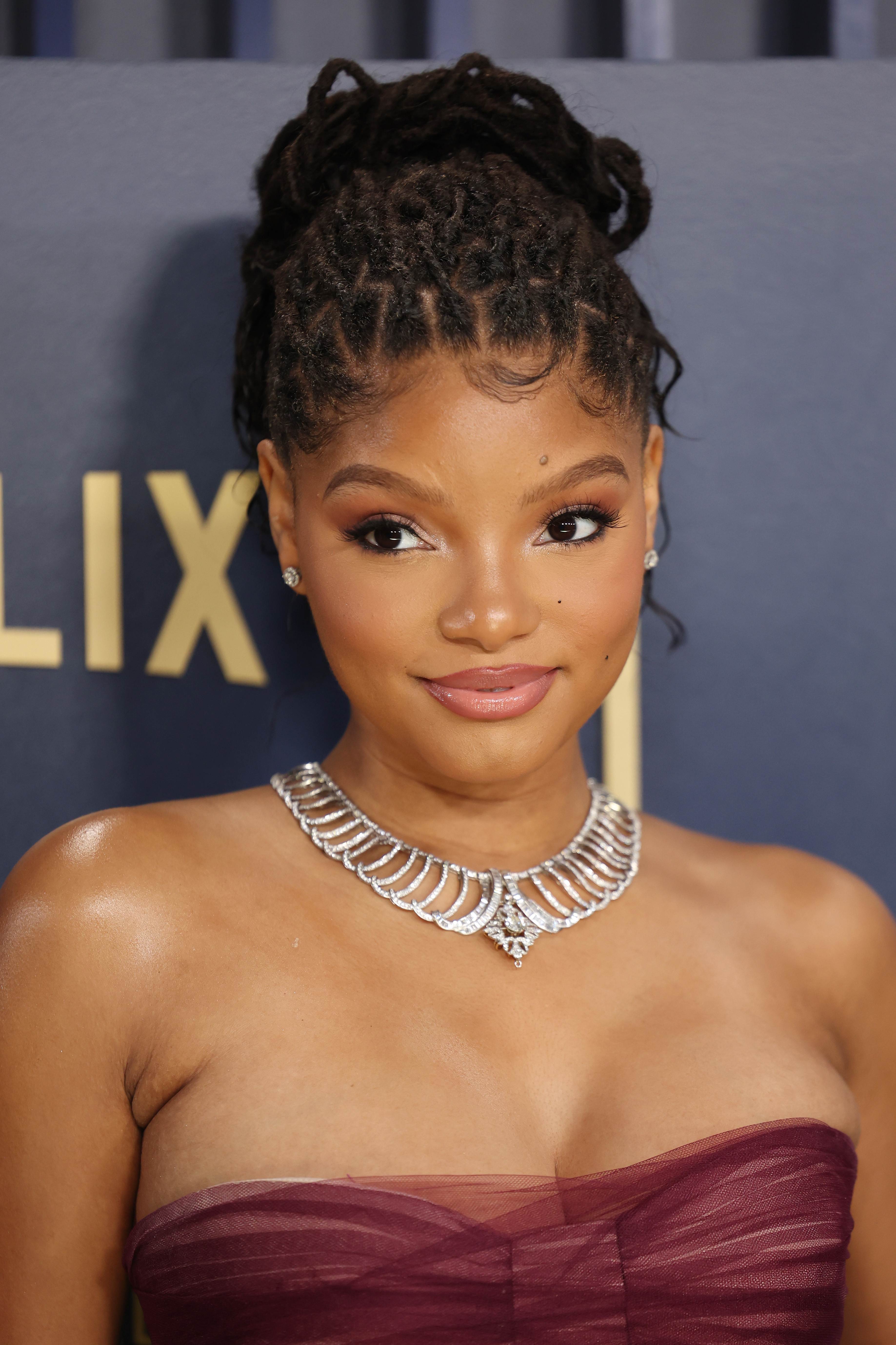 Halle Bailey poses on a red carpet wearing a strapless dress and a statement necklace