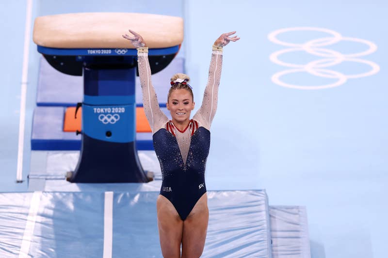 Gymnast in a leotard performs on the vault at the Tokyo 2020 Olympics, with arms raised and a confident smile