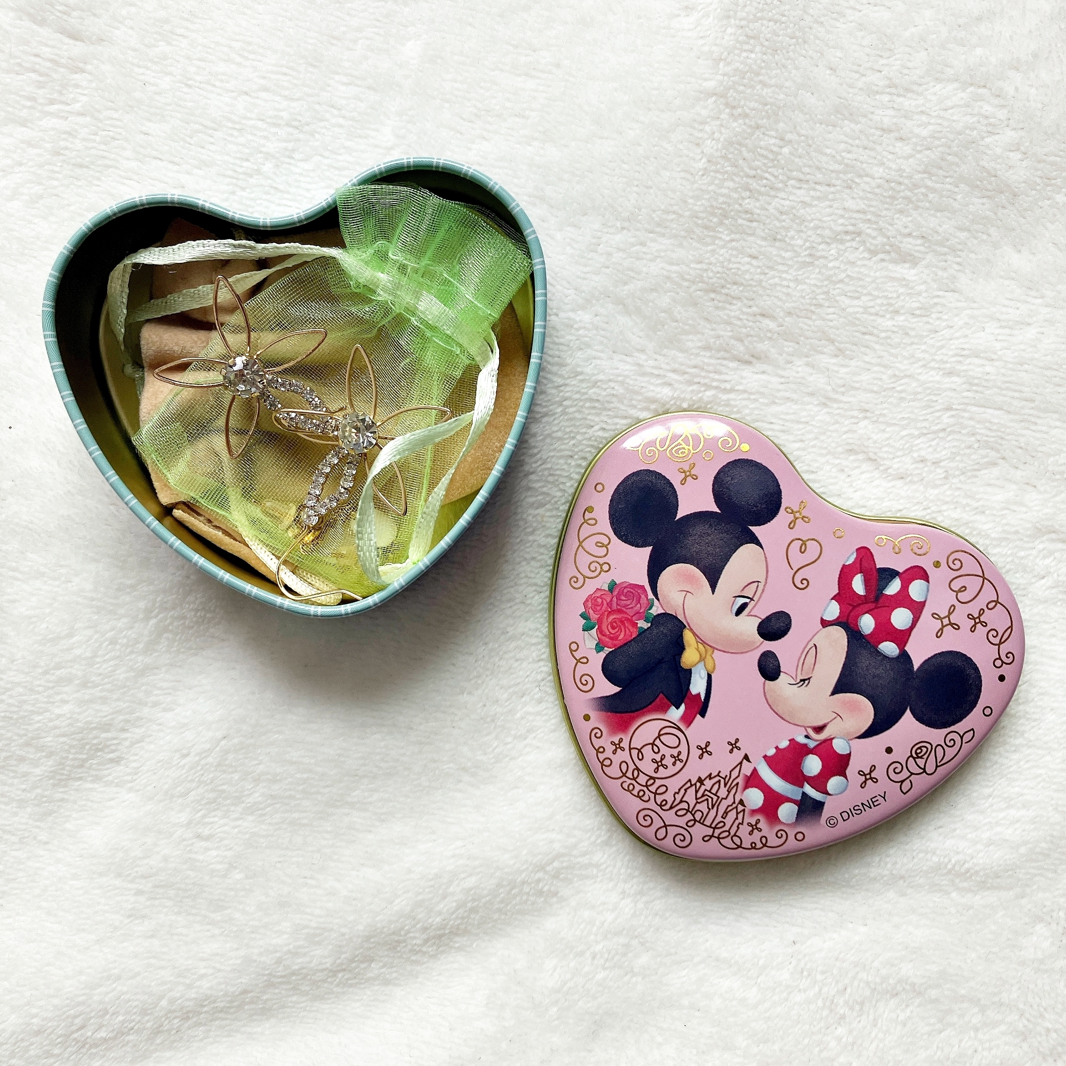 ハート型の缶のふたにミッキー・マウスとミニー・マウスの絵が描かれており、開いた缶の中にはアクセサリーが入っています。