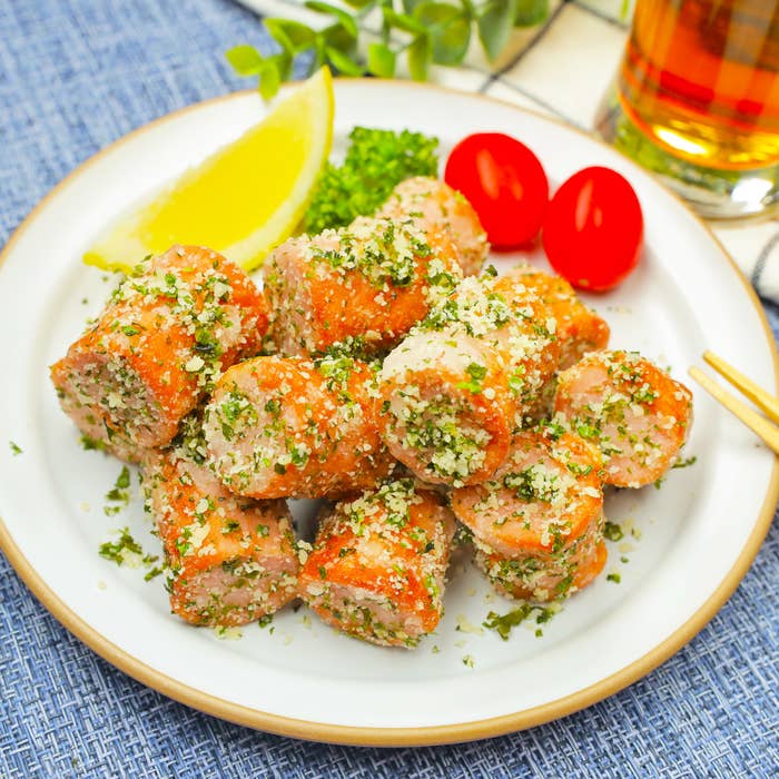 皿に盛られた青のりとチーズがまぶされた魚肉ソーセージの料理。レモンとトマトの飾り付き。