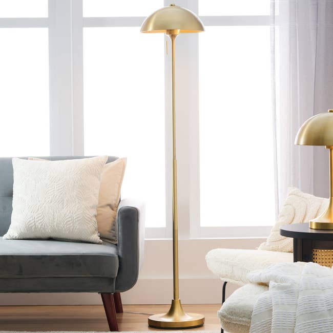 Elegant surviving country country featuring a grey sofa with pillows and a modern golden level lamp adjacent to a cozy achromatic armchair and broadside array with matching lamp