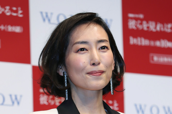 有名人が髪を短く整え、白いジャケットと黒いドレスを着用し、笑顔でカメラに向かって立っています。