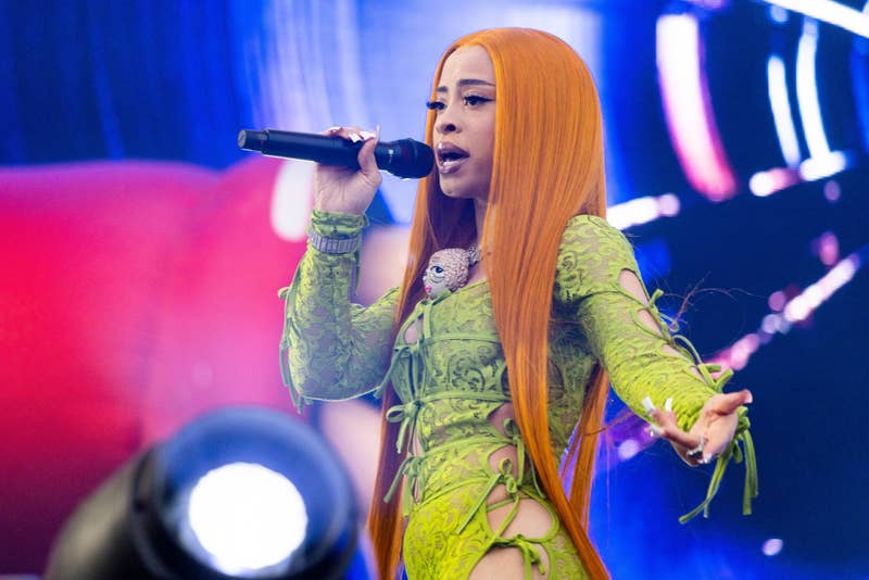 Ice Spice performing on stage, wearing a stylish green outfit with lace-up details, holding a microphone, and singing passionately