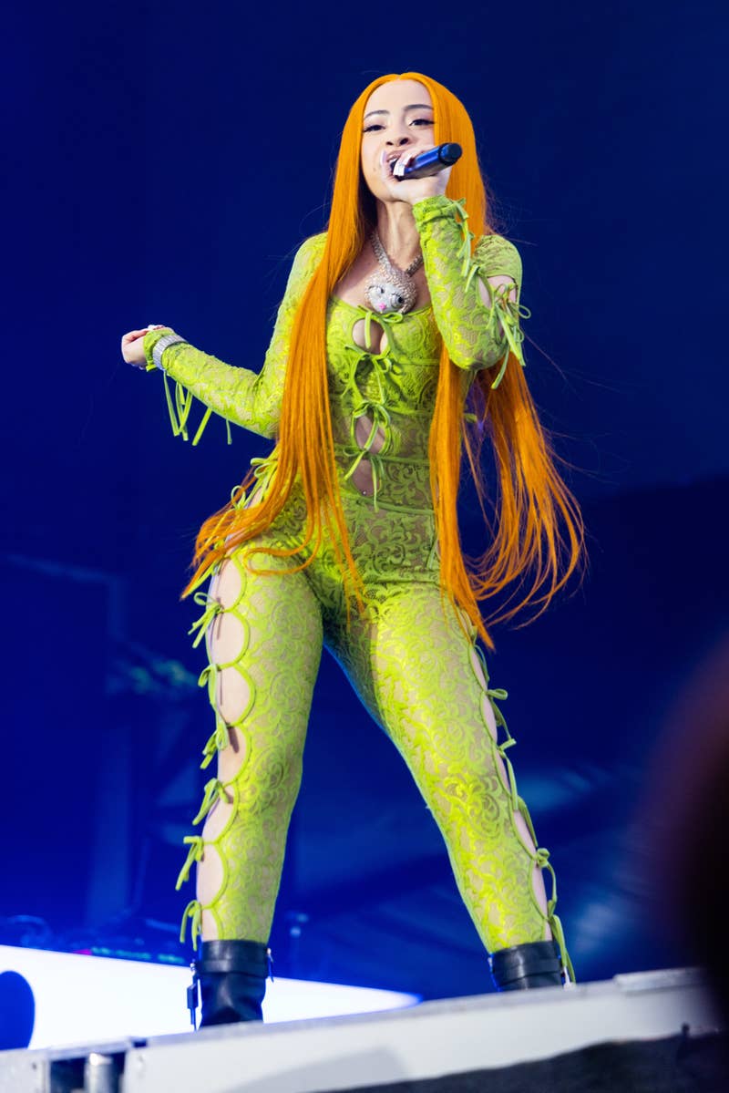 Ice Spice performs on stage wearing a stylish lace jumpsuit with intricate cutouts and long flowing hair while holding a microphone