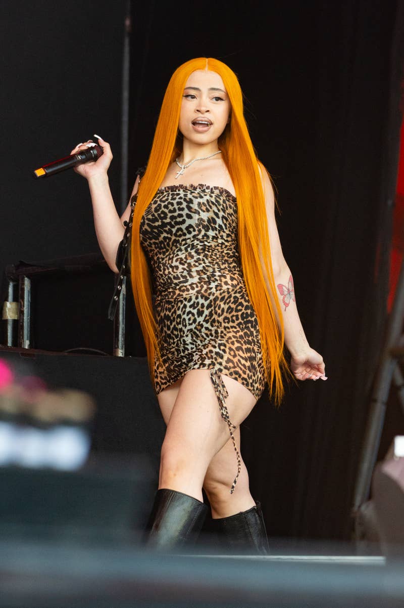 A woman, wearing a form-fitting leopard print dress and boots, holds a microphone while performing on stage