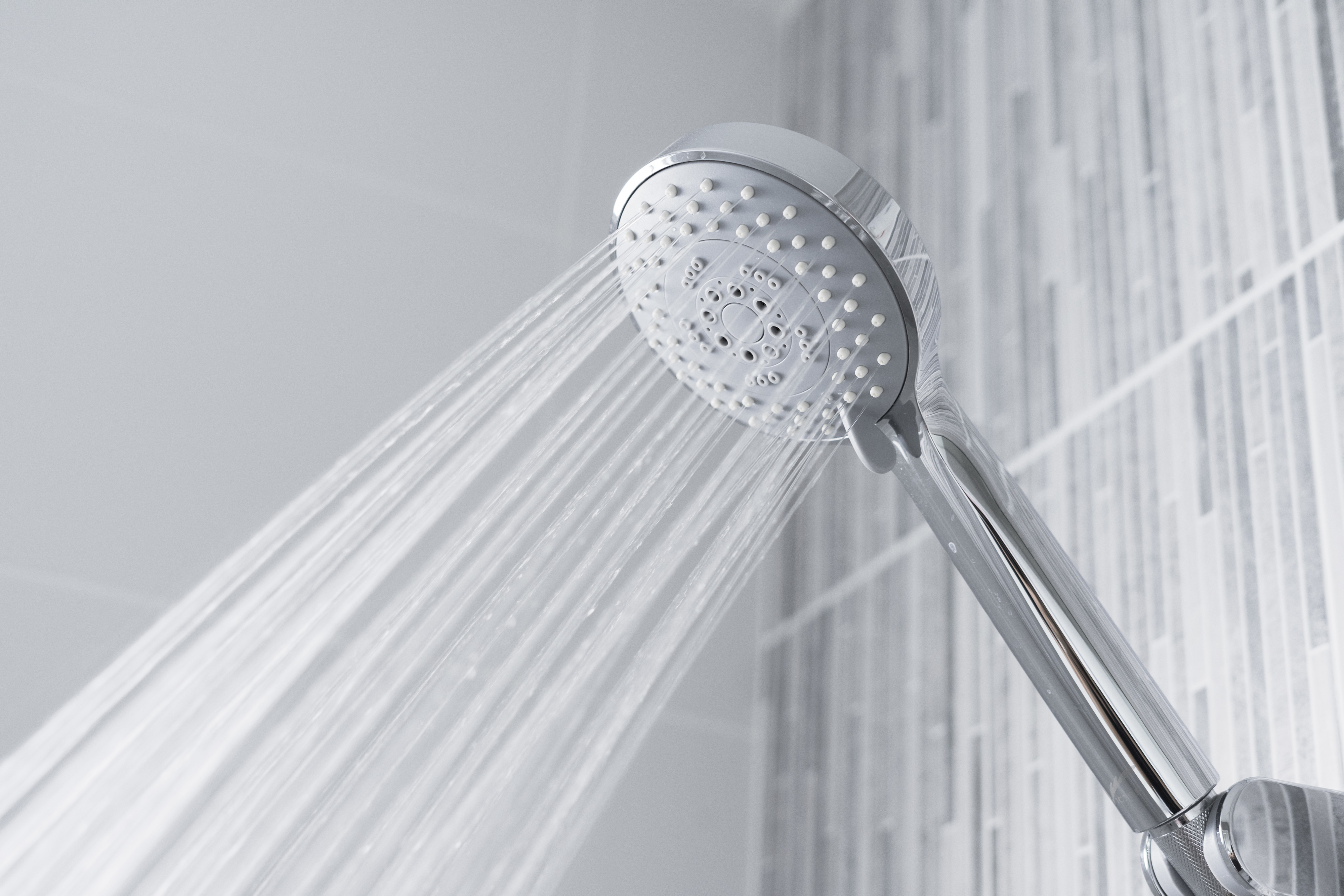 Water streams from a handheld showerhead in a modern tiled shower