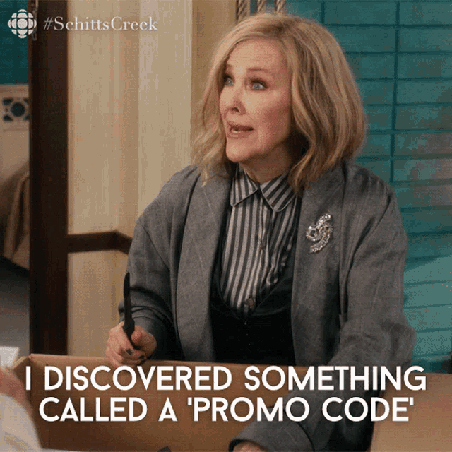 Catherine O'Hara as Moira Rose in Schitt's Creek, dressed in a stylish gray blazer over a striped shirt, excitedly stating, &quot;I discovered something called a 'promo code'&quot;