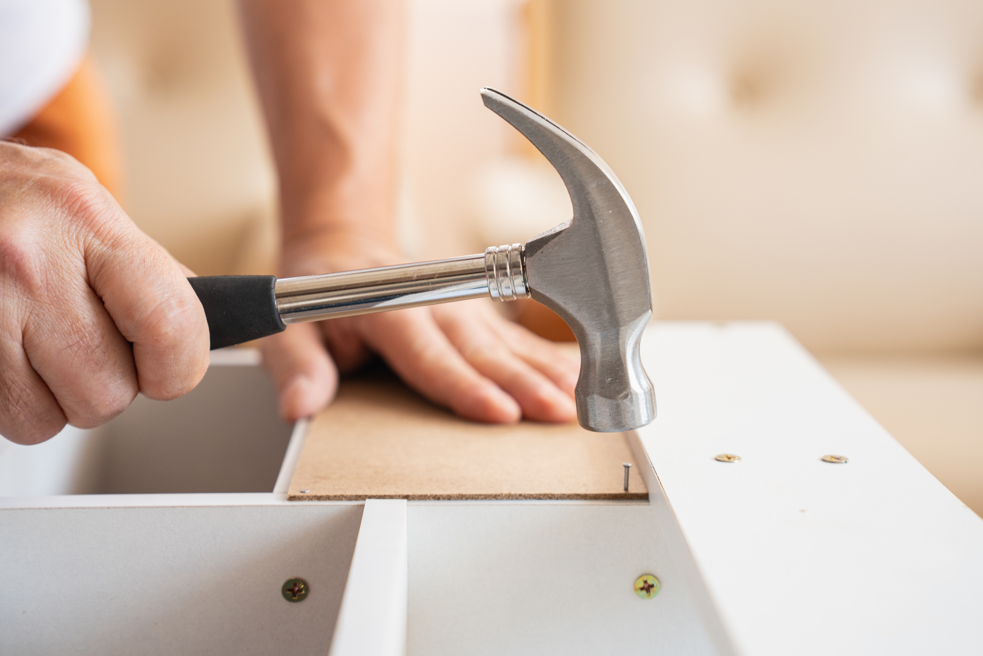 A close-up of a person’s hands hammering a nail into a piece of wood during a construction or assembly project