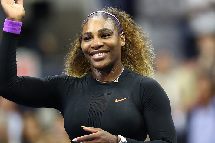 Serena Williams waves and smiles while wearing a sleek athletic outfit at a public event