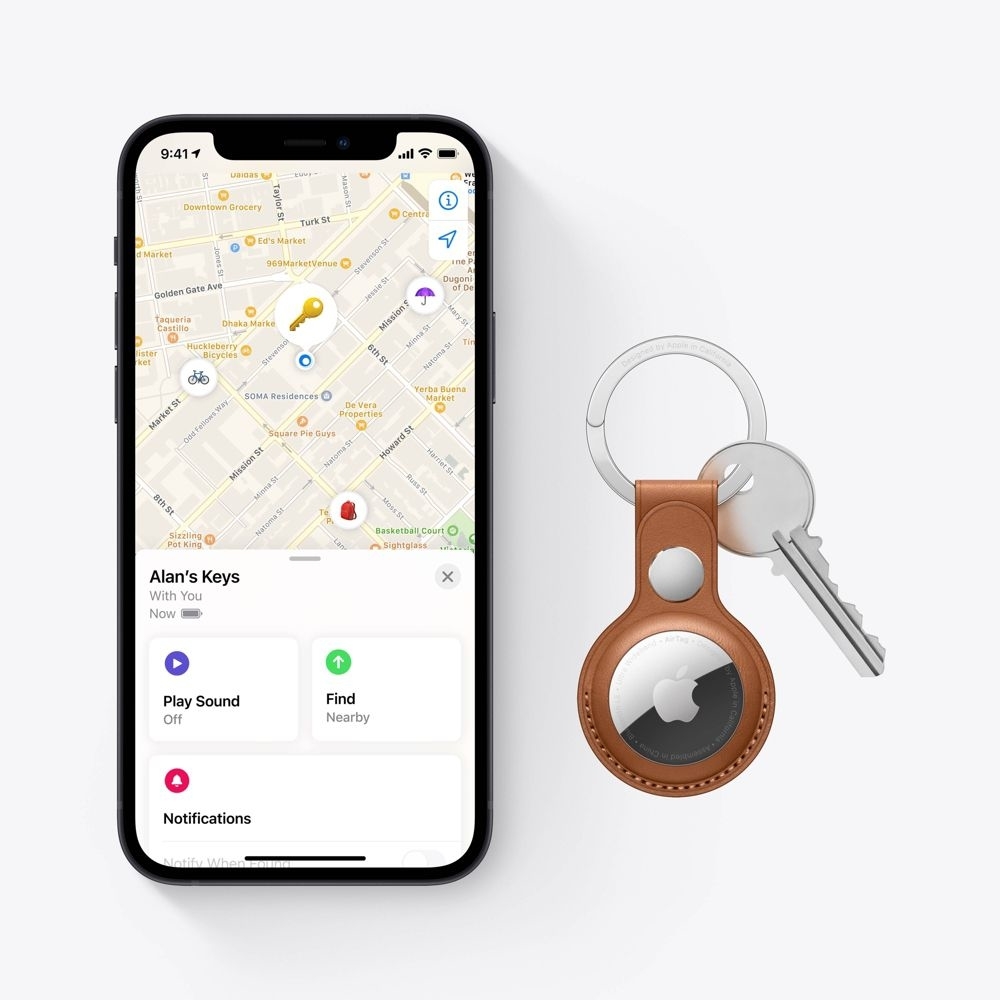 iPhone with map and AirTag tracker in leather holder attached to keys. The phone screen shows a map with "Alan's Keys" located. The article is about shopping