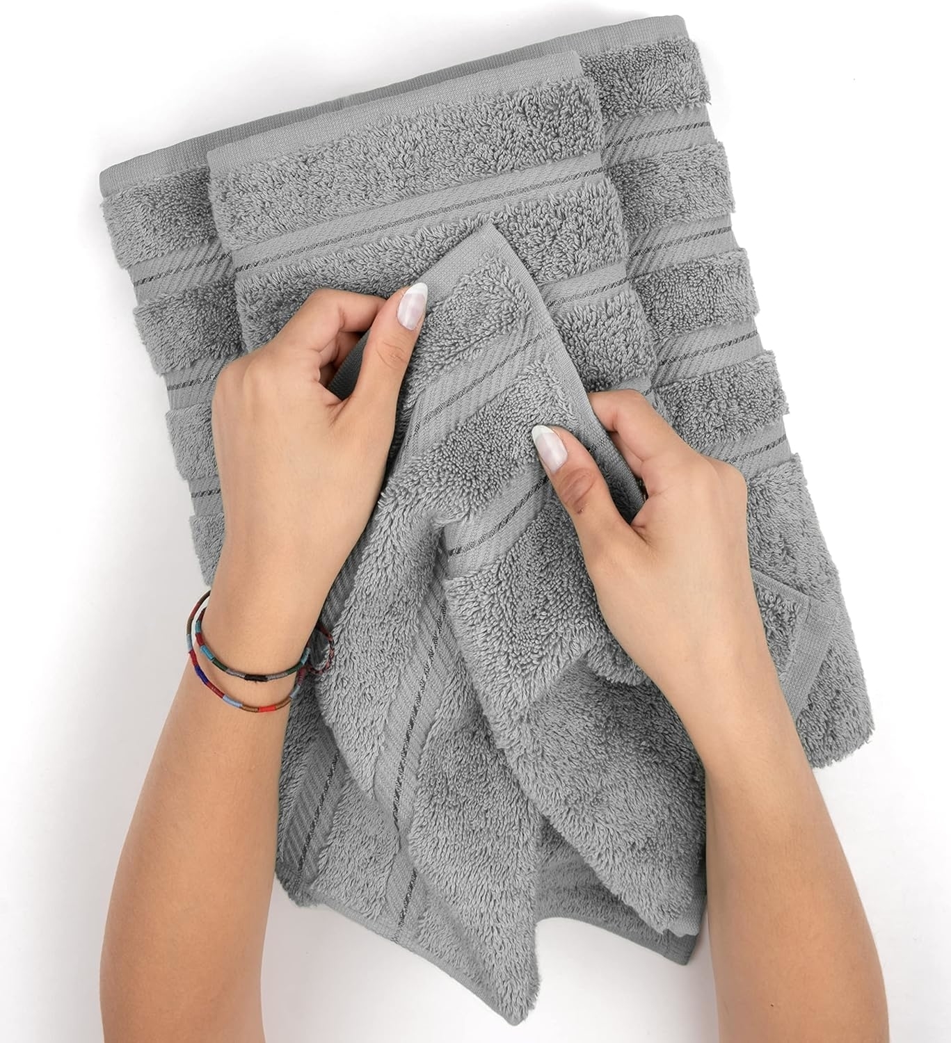 A person with manicured nails examining a gray towel among a stack of similar towels. The image is used in a shopping article
