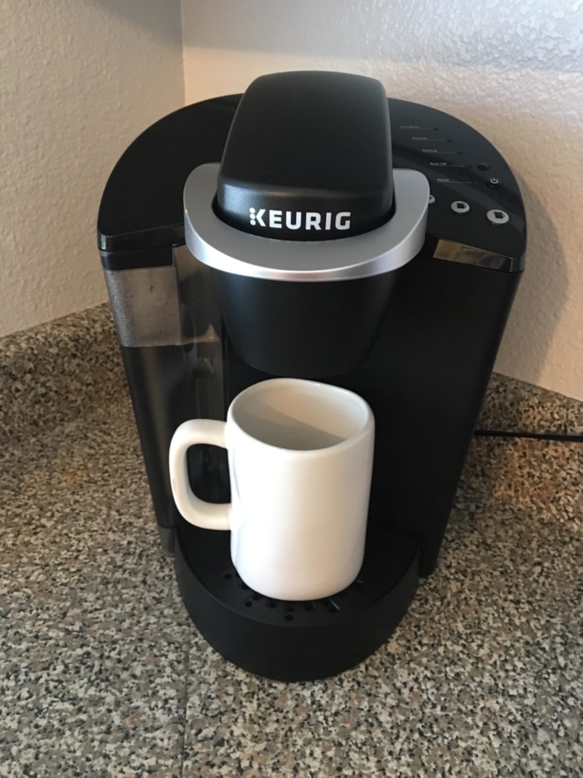 Keurig coffee maker on a countertop with a white mug placed under the dispenser