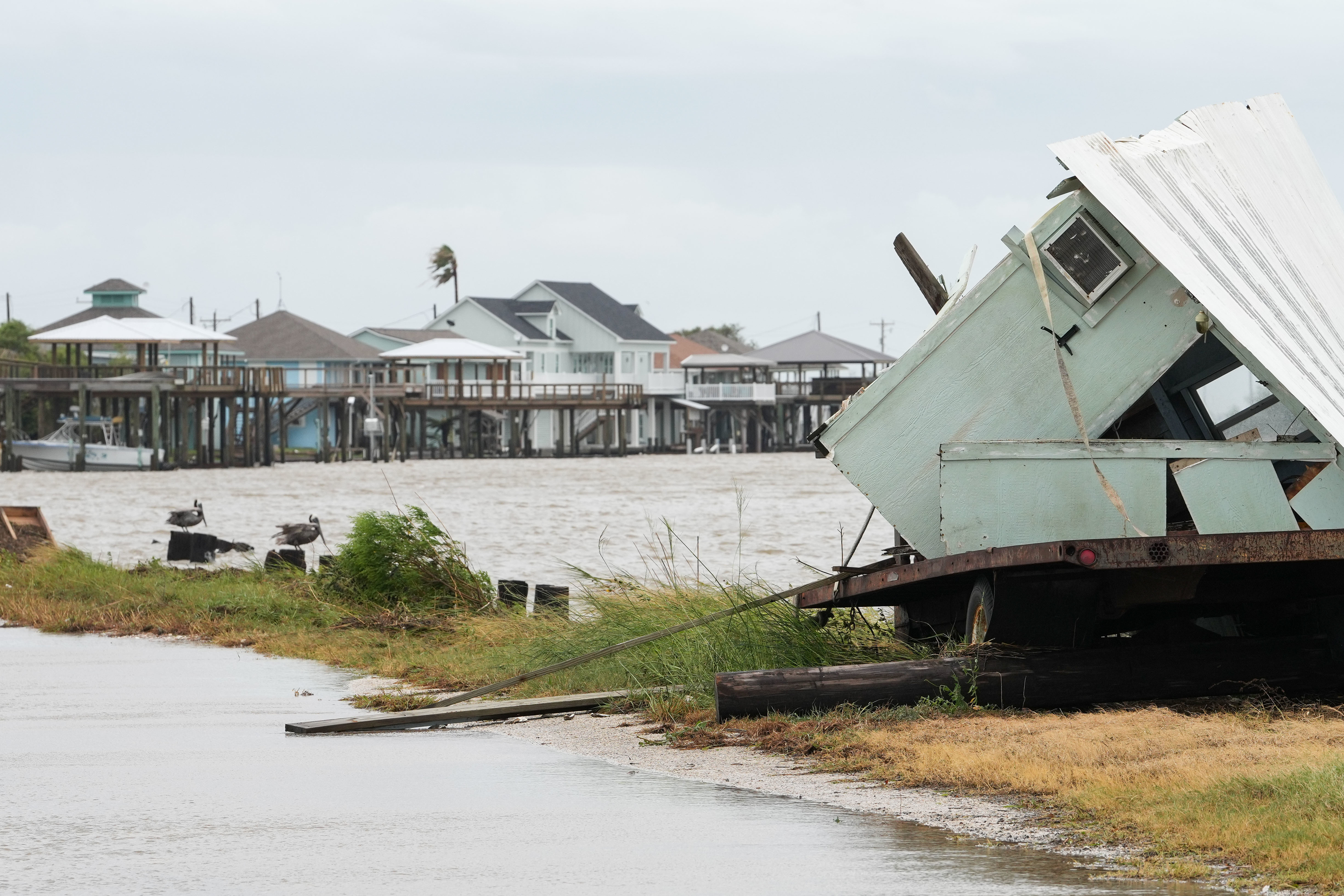 Damaged house displaced onto a road in a coastal area after a severe storm. Elevated houses in the background remain intact