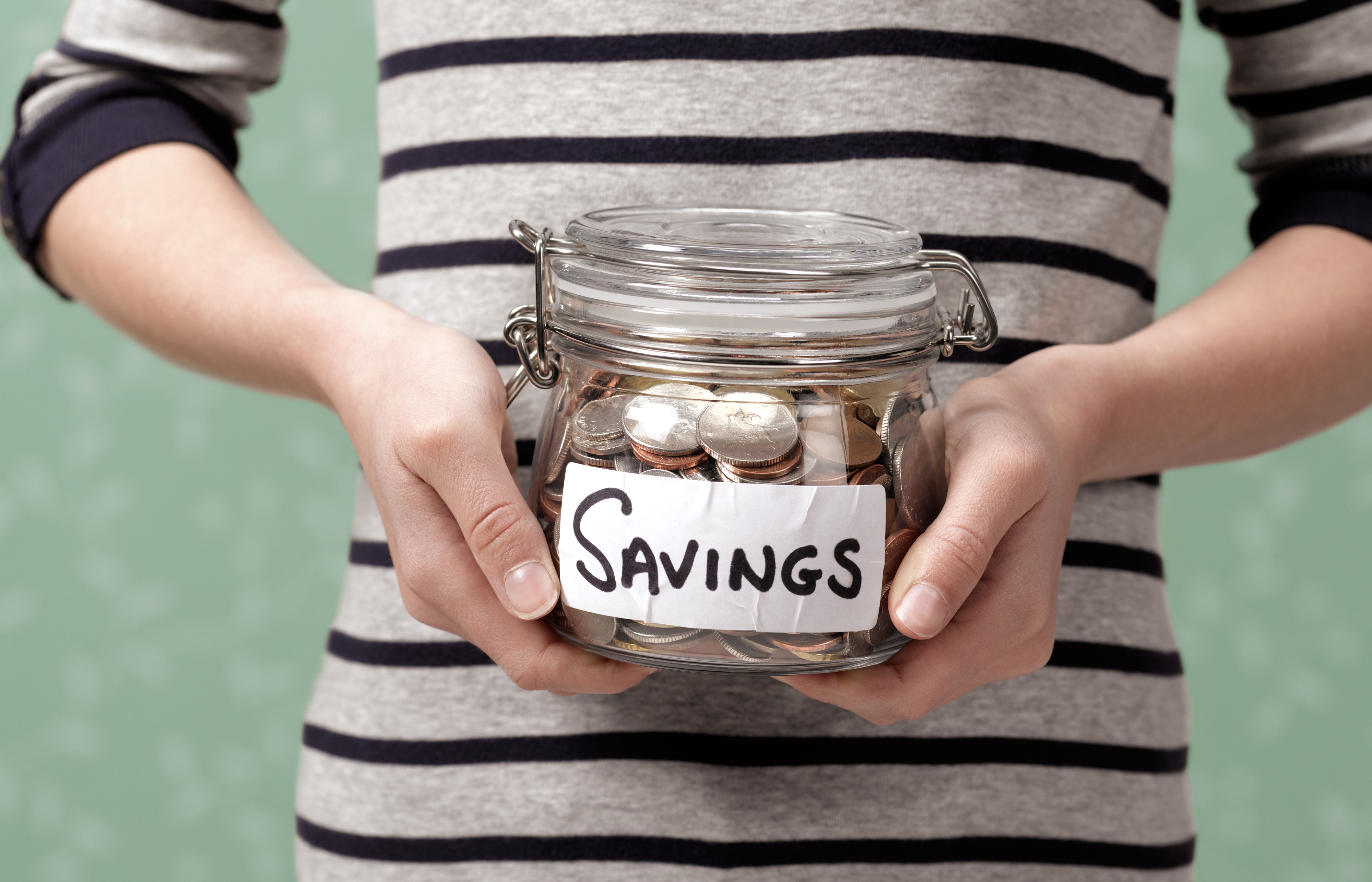 Person holding a glass jar labeled "SAVINGS" filled with coins and bills