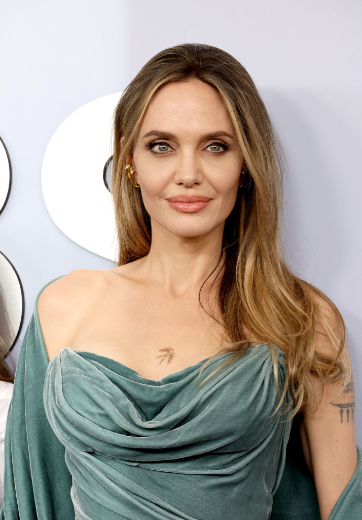Angelina Jolie on the red carpet, wearing a draped, off-the-shoulder dress with tattoo visible on chest