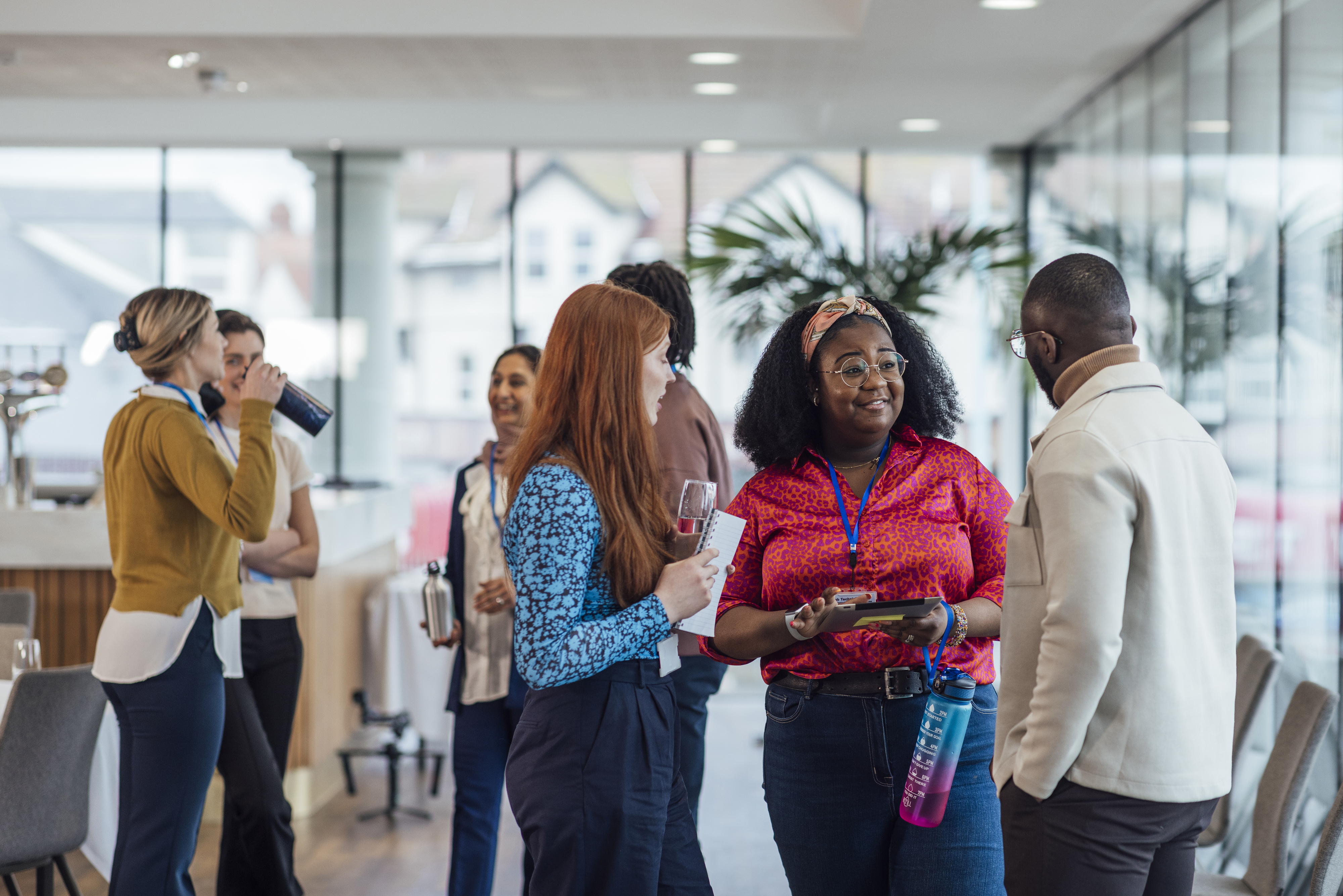Group of coworkers talking and mingling in a modern office setting, holding drinks and interacting informally