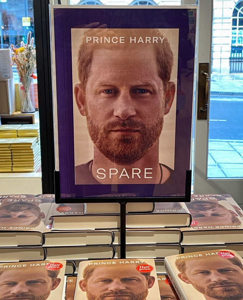 Cover of "Spare" by Prince Harry is displayed above stacks of the book in a store. Prince Harry's face is on the cover