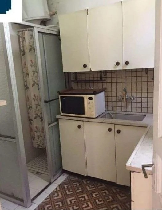 Small, compact kitchen with a microwave on the counter, a sink, and metal shelving above. A narrow shower stall with a floral curtain is adjacent to the kitchen area