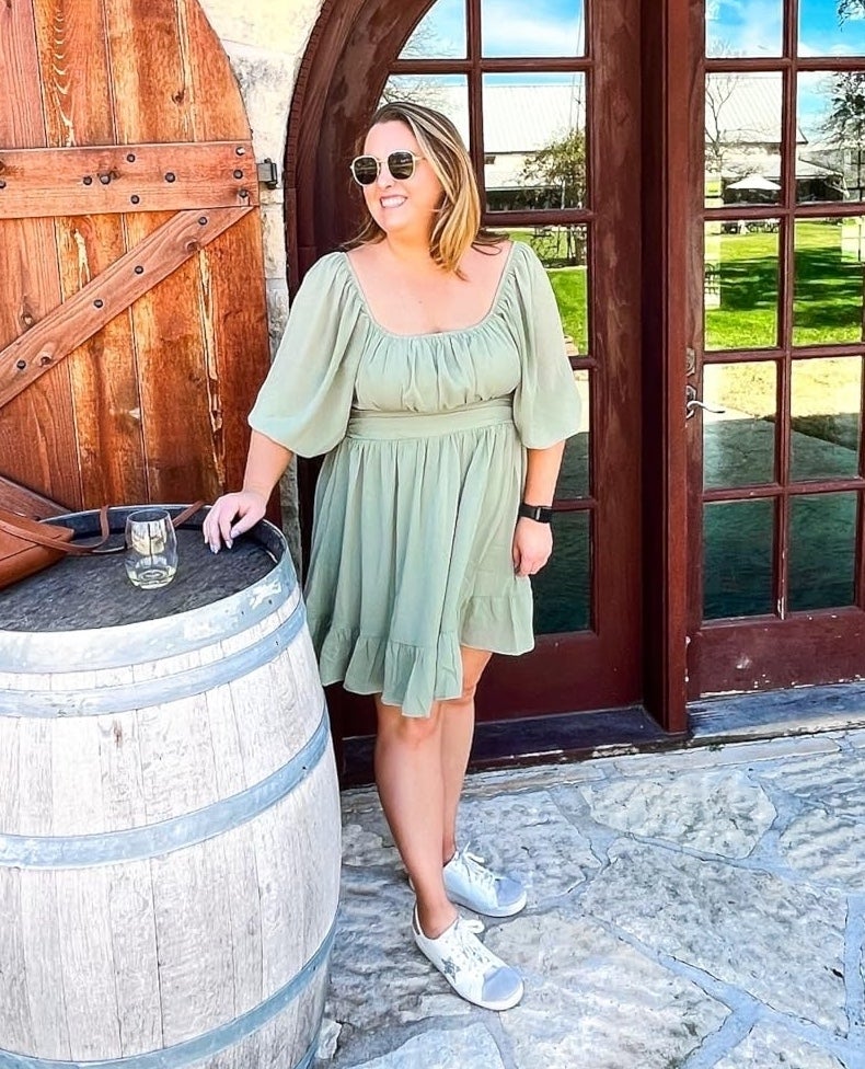 a reviewer wearing the light sage green dress at a winery