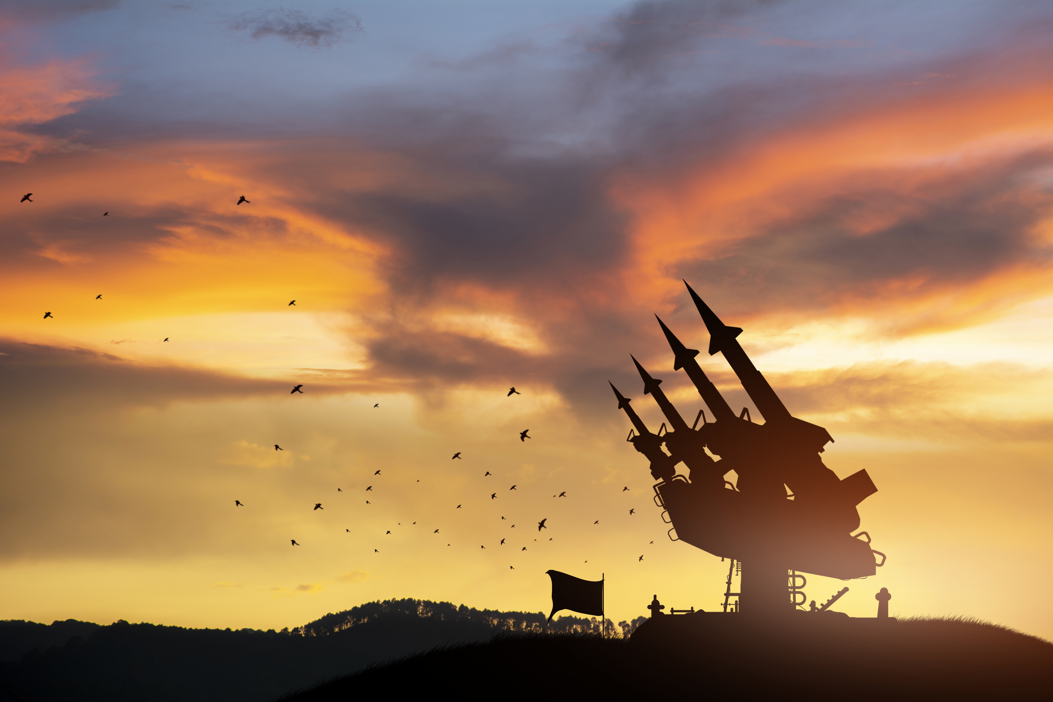 Silhouette of an anti-aircraft missile system against a dramatic sunset sky with birds flying around