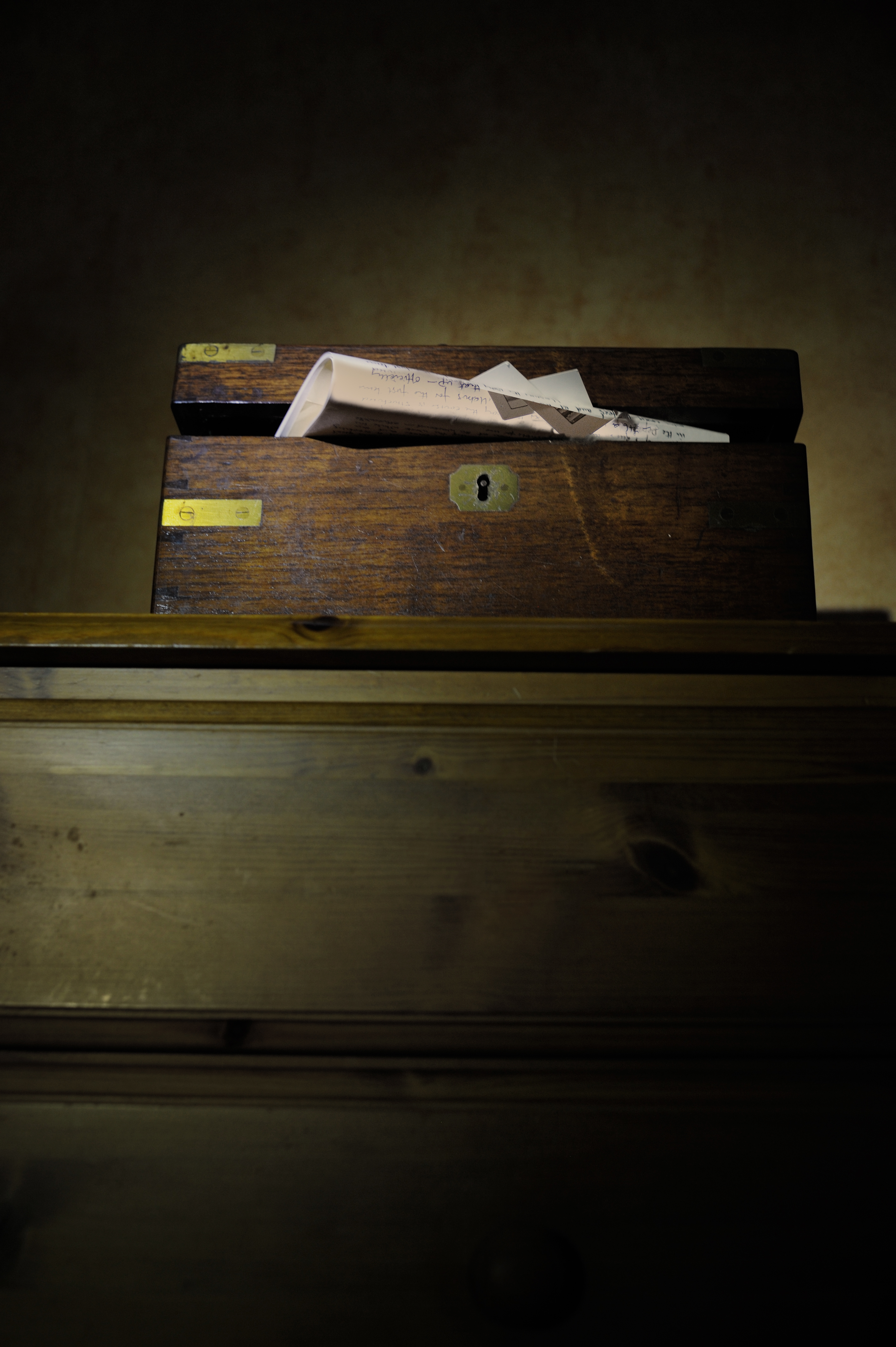 A wooden lockbox with a paper folded into a small aircraft resting on its lid, placed on top of a wooden cabinet