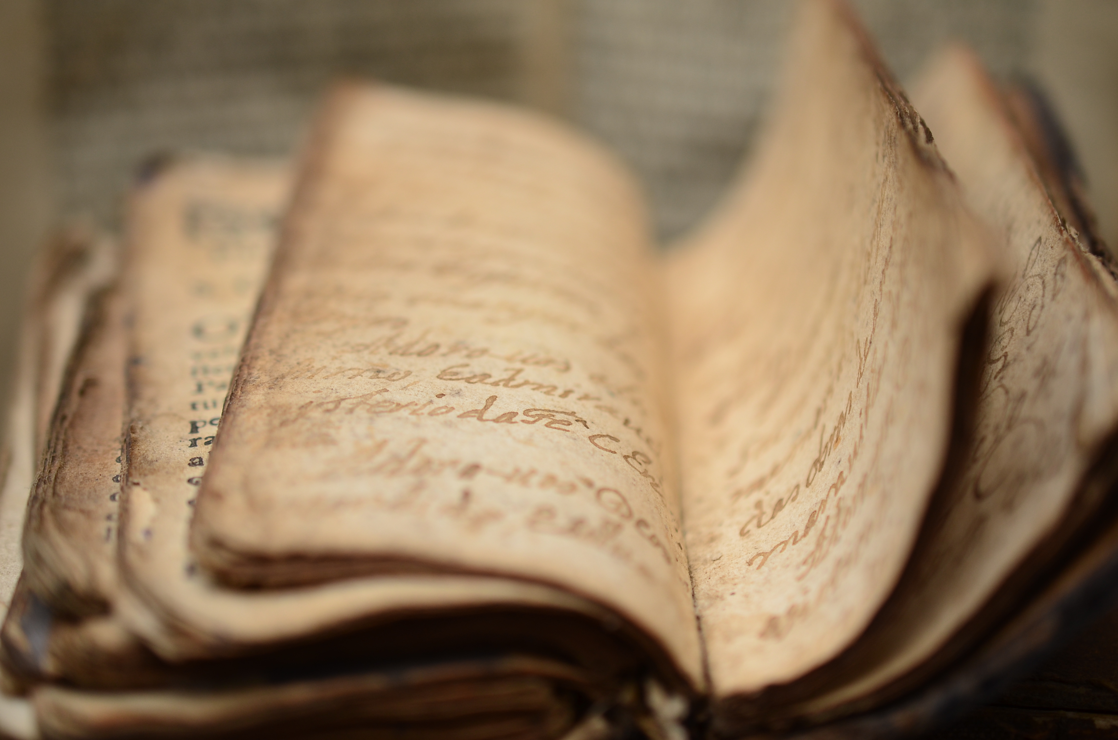 A close-up photo of an old, worn book with visibly aged and partially illegible handwritten text on its pages