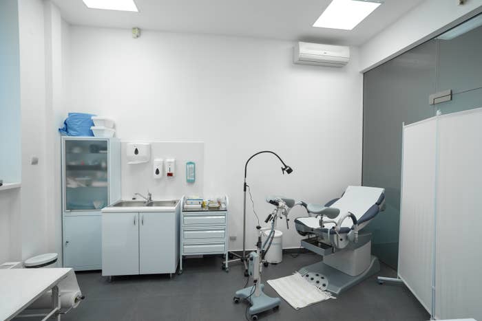 Medical examination room with a gynecological chair, a sink, storage cabinets, and medical equipment