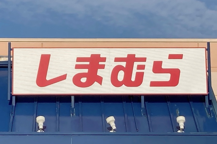 The image shows the exterior of a Shimamura store, a Japanese retail chain, with its name in red Japanese characters on a sign above the entrance