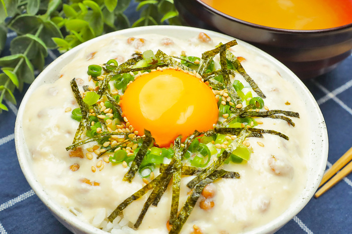 ご飯の上にとろろと生卵が乗ったどんぶり料理と味噌汁がテーブルに置かれている。