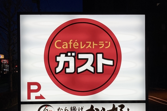 夜のガストの看板が写っており、カフェレストランガスト、からあげ専門 から好しの文字が見えます。