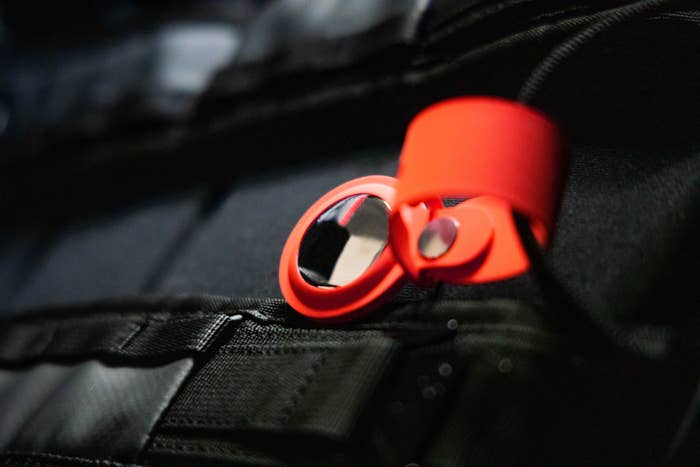 Close-up of an orange airtag attached to a black backpack