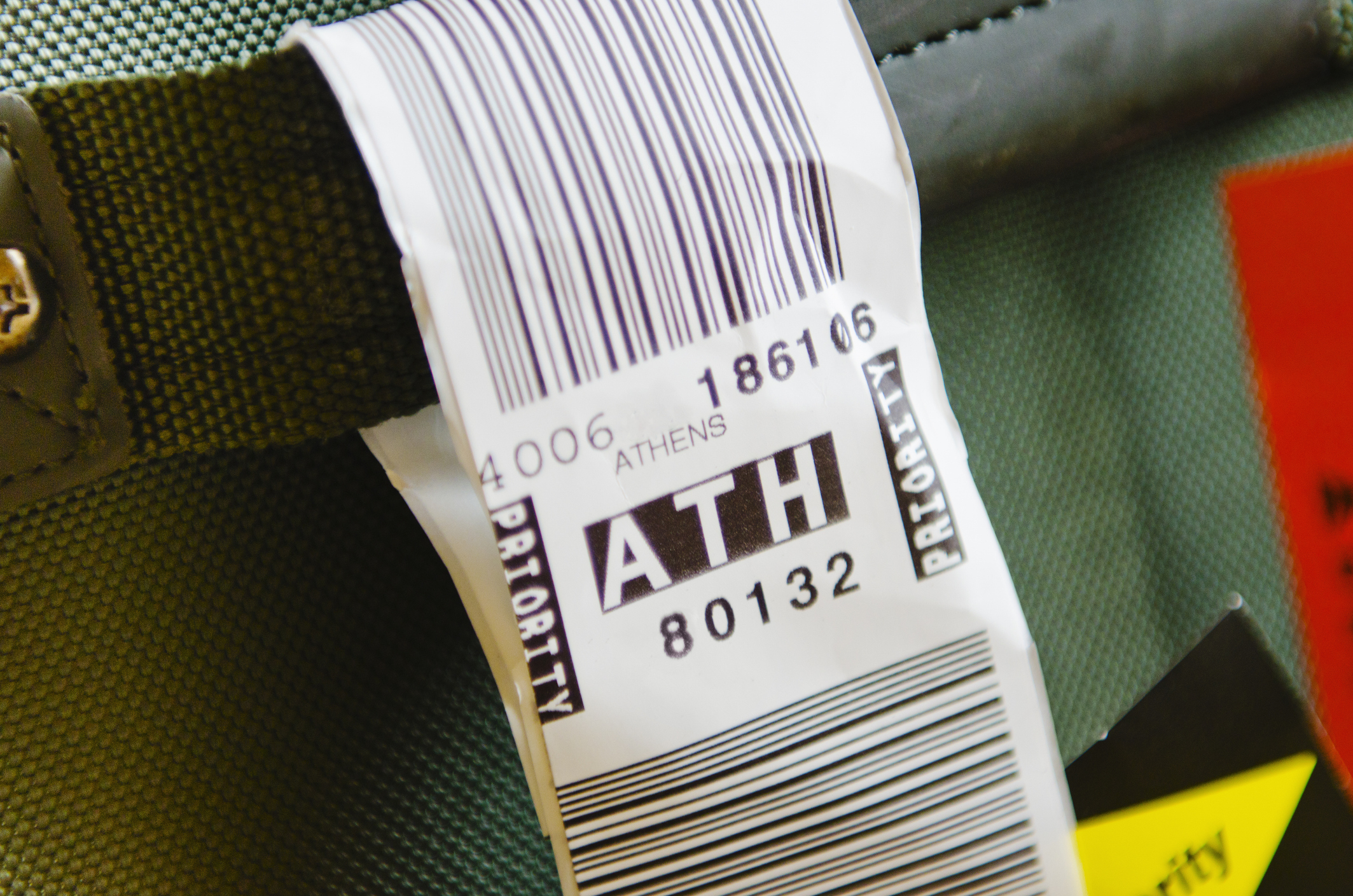 Luggage tag with the code &quot;ATH&quot; for Athens attached to a suitcase handle. The tag includes a barcode and priority markings