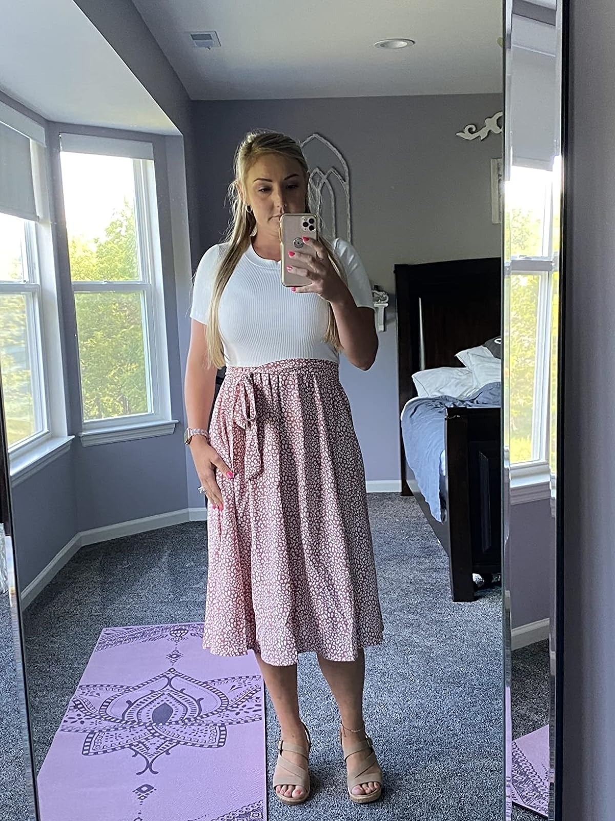 A reviewer takes a mirror selfie wearing the dress with a white top and a pink and white patterned skirt and sandals