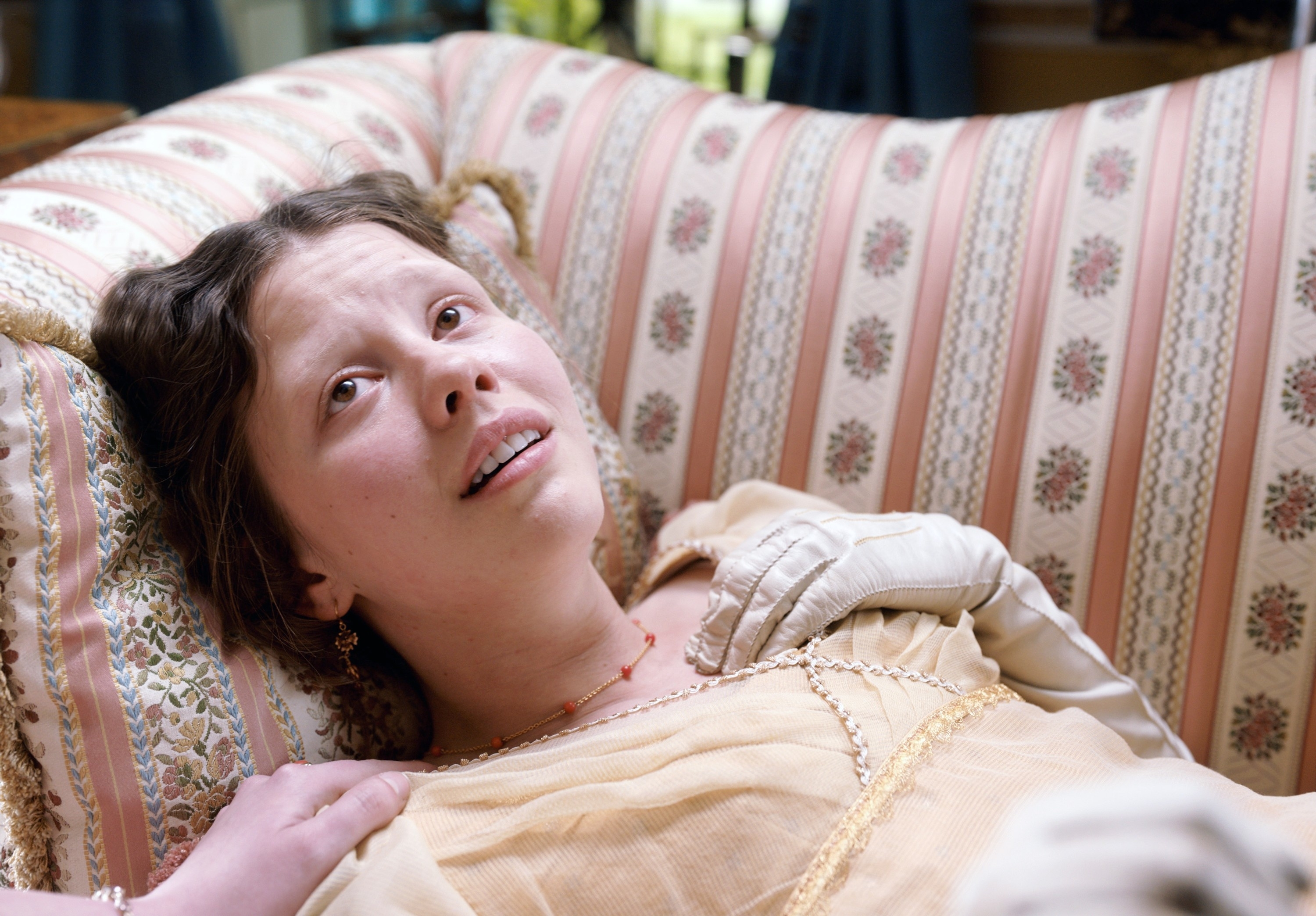 Mia Goth on a patterned couch in a scene from "Emma"