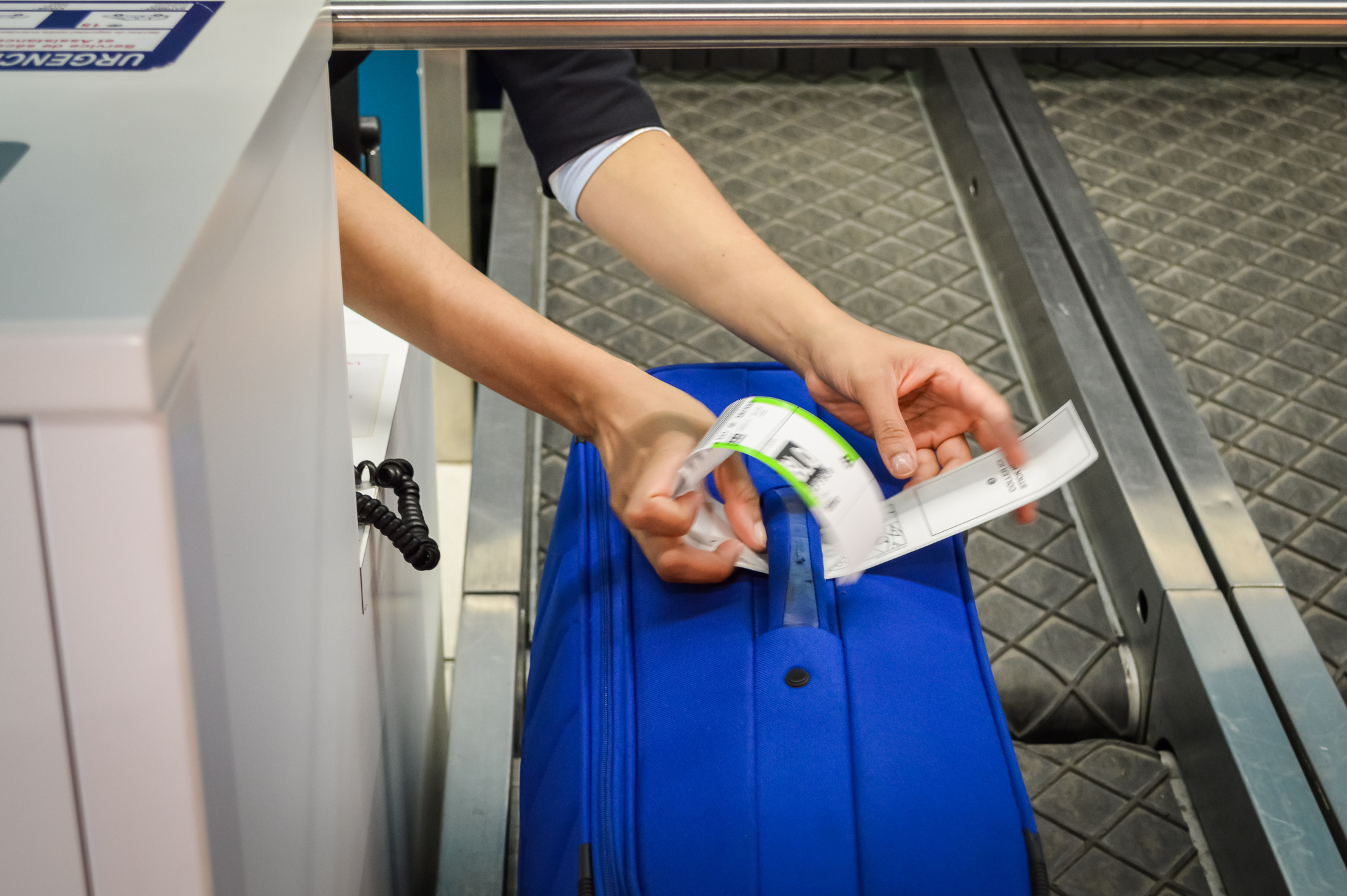 An airline staff member places a luggage tag on a blue suitcase at a check-in counter