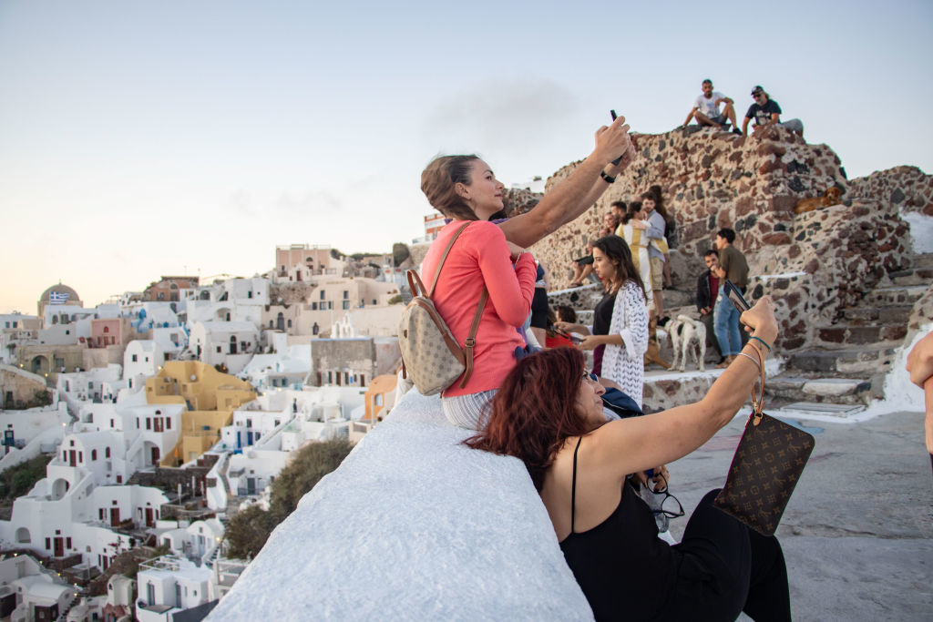 People taking selfies and enjoying the sunset with views of white-washed buildings and the sea in Santorini, Greece
