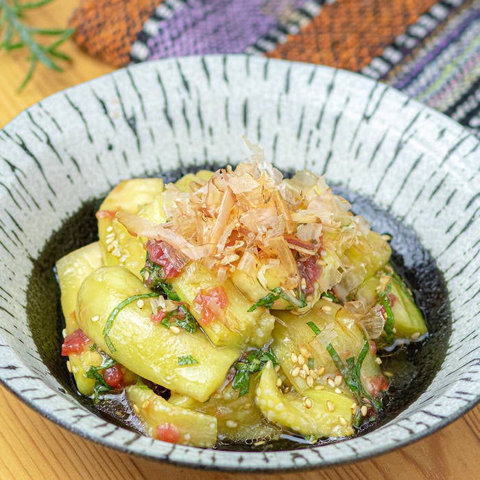 器に盛られた、美しく調理されたなすと梅肉の料理。野菜の中にはゴマの種が散らばり、かつお節が飾られている。