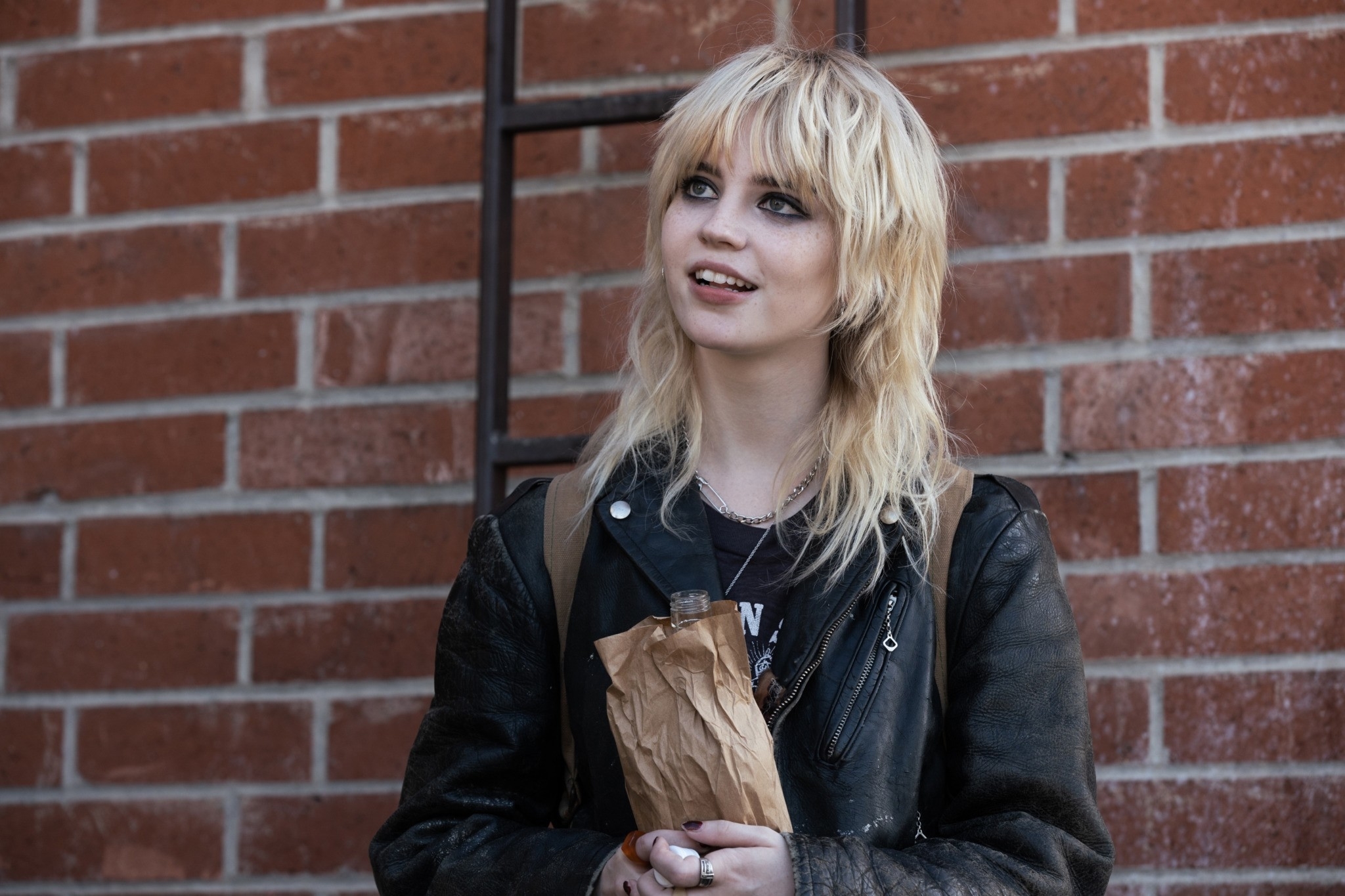 Sophie Thatcher with a shag haircut and leather jacket in front of a brick wall in a scene from "Yellowjackets"