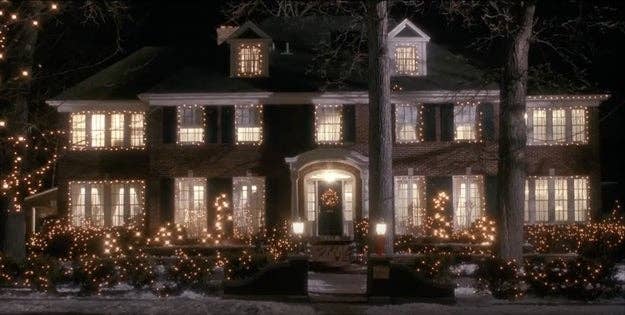 Large house with festive holiday lights decorating the windows and surrounding area at night. Snow covers the ground