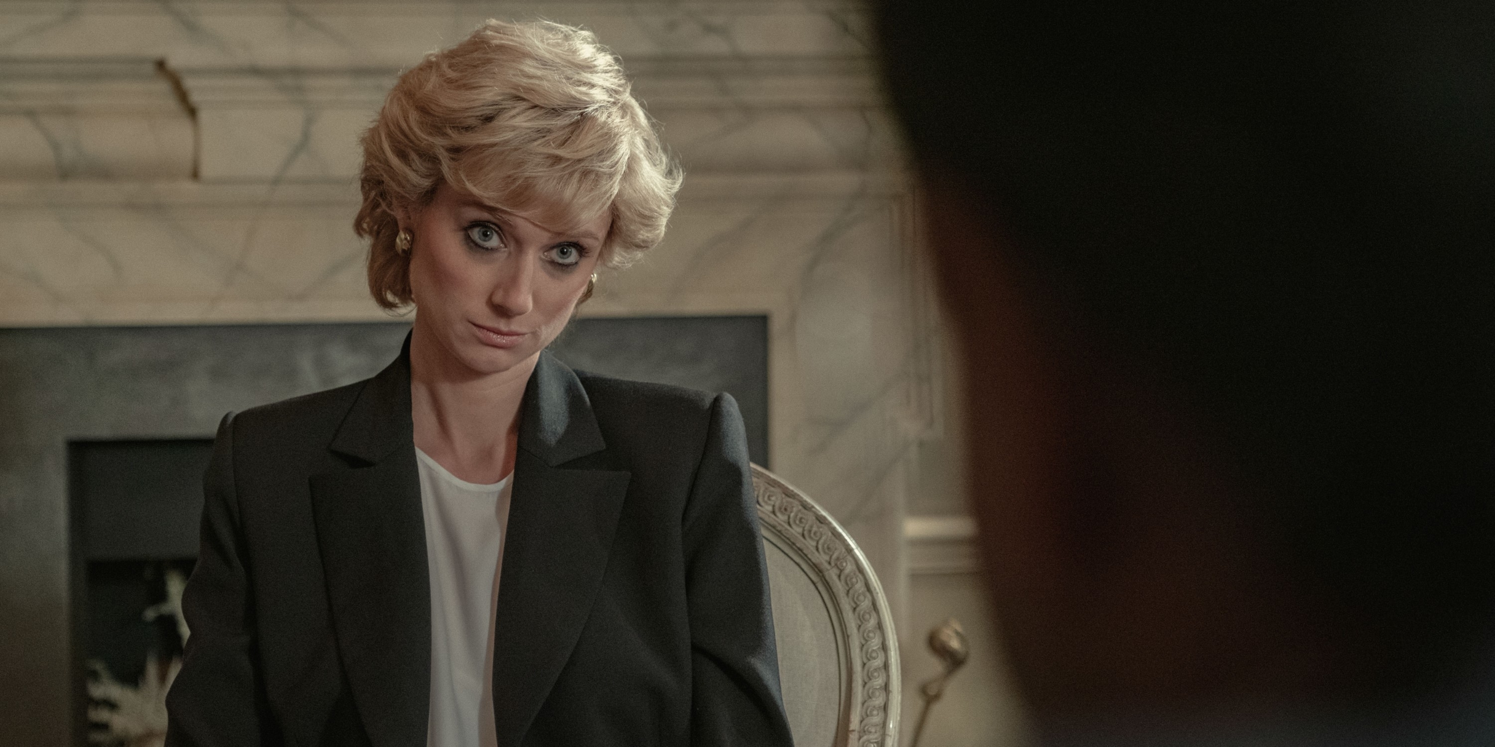 Elizabeth Debicki portrays Princess Diana, wearing a formal black blazer and white blouse, in a scene from "The Crown"
