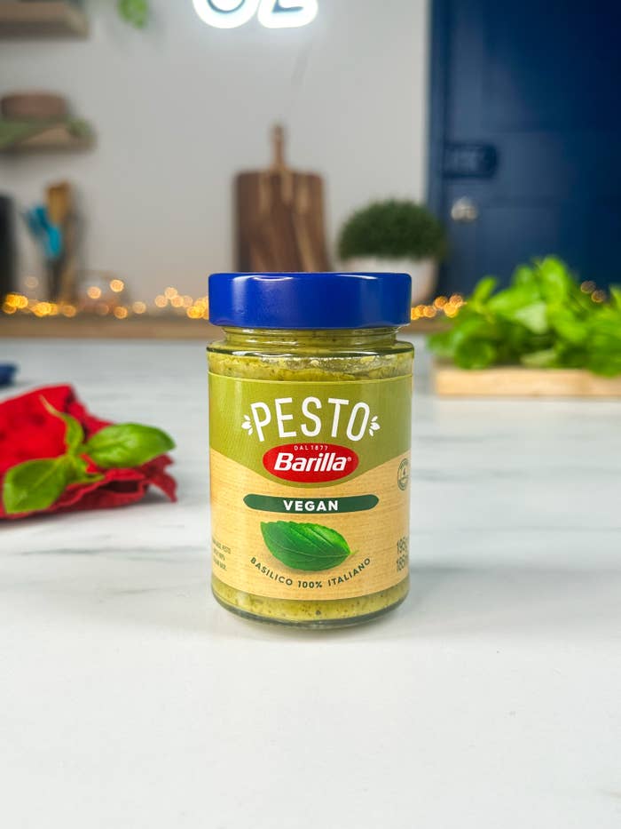 Barilla Vegan Pesto jar on a kitchen counter with herbs and utensils in the background