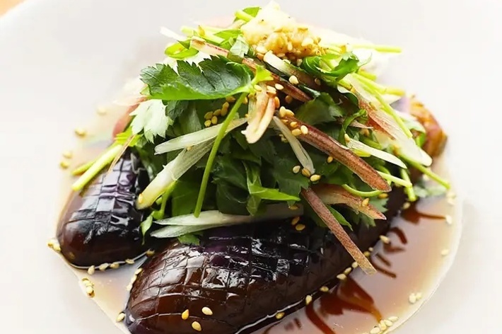 皿に盛り付けられた茄子の料理、タレがかかり、薬味と香草がトッピングされています。