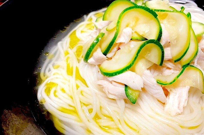 黒いお皿に盛り付けられた冷やし中華そば。薄切りのズッキーニと千切りの鶏肉がトッピングされている。背景にレモンが見える。