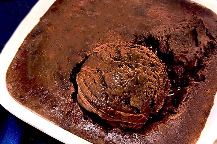 スクエア型の白い皿に盛り付けられたチョコレートブラウニーの写真。中央にはアイスクリームのようなトッピングが見られる。