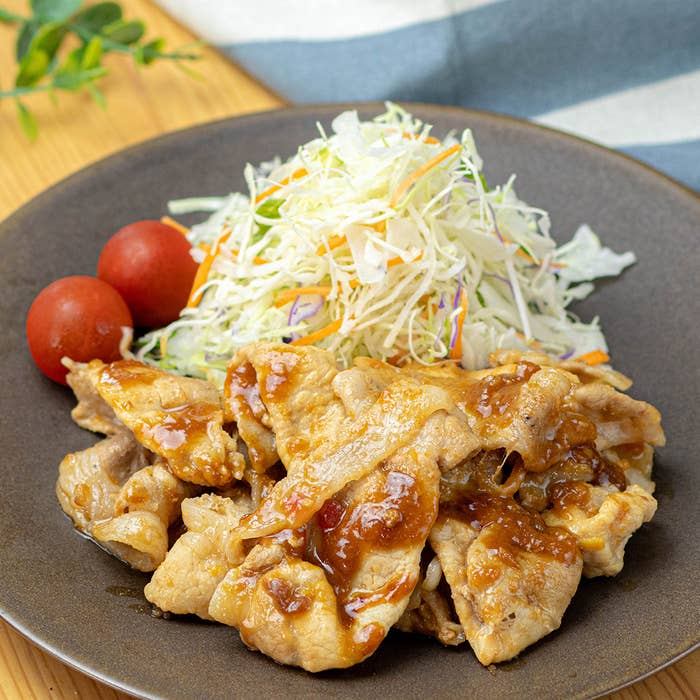 皿に盛られた豚肉炒め、付け合わせにキャベツの千切りとミニトマトが乗っています。