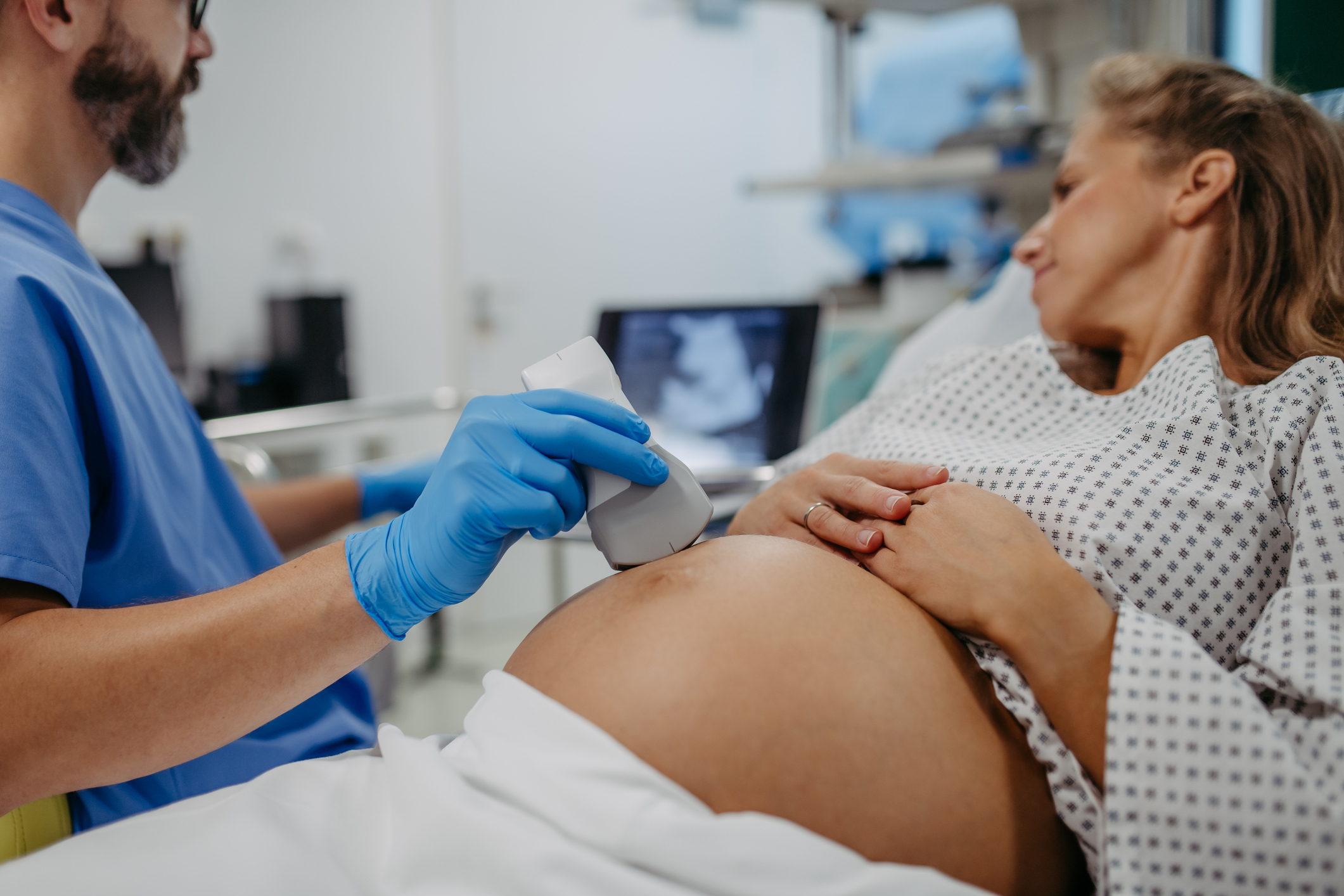 A doctor performs an ultrasound on a pregnant patient's abdomen while she lies on an examination bed in a medical setting