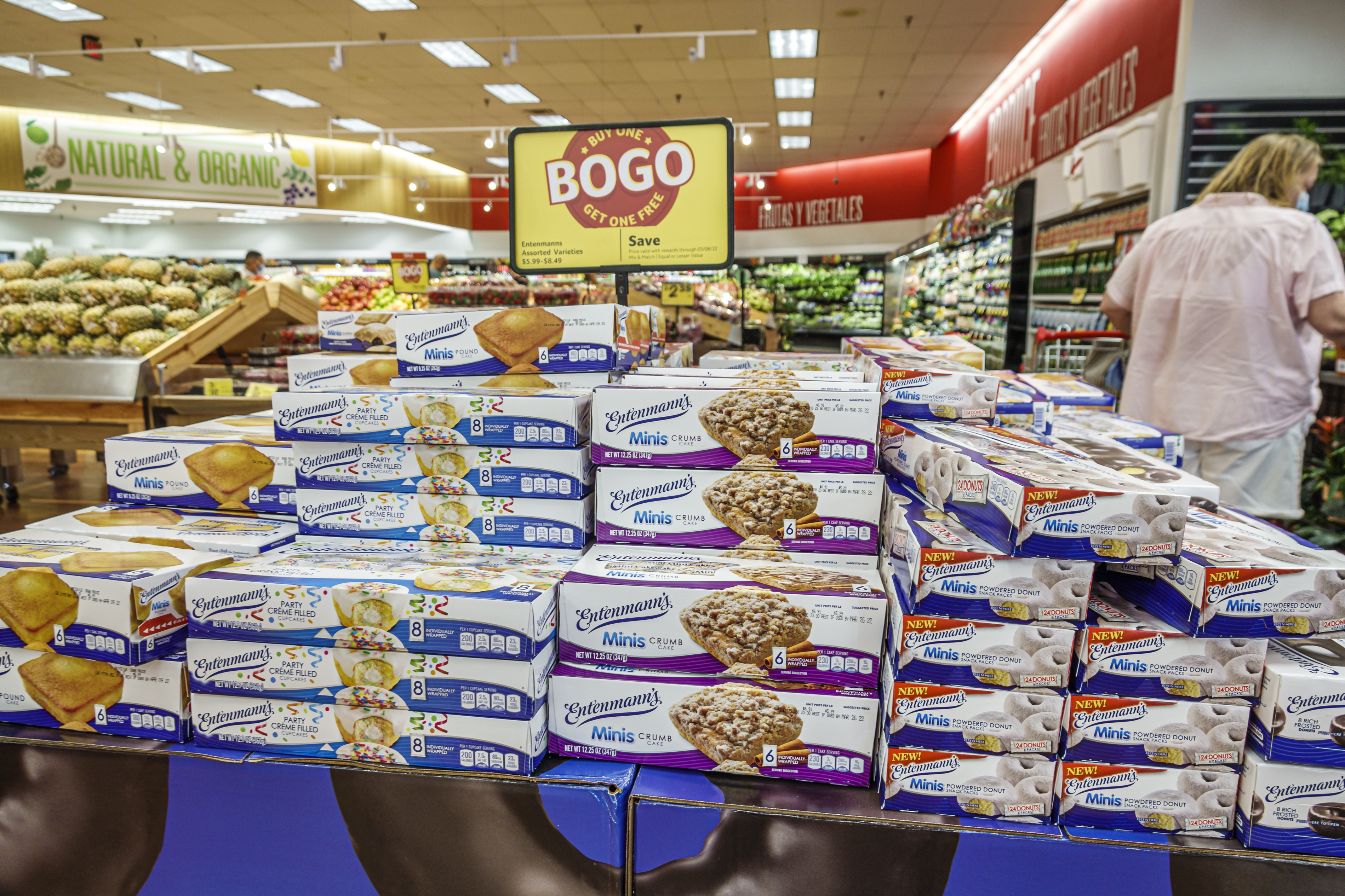 Store display of Entenmann's Minis baked goods with a BOGO (Buy One Get One Free) sign. Shelves are stocked with various snacks in a grocery aisle