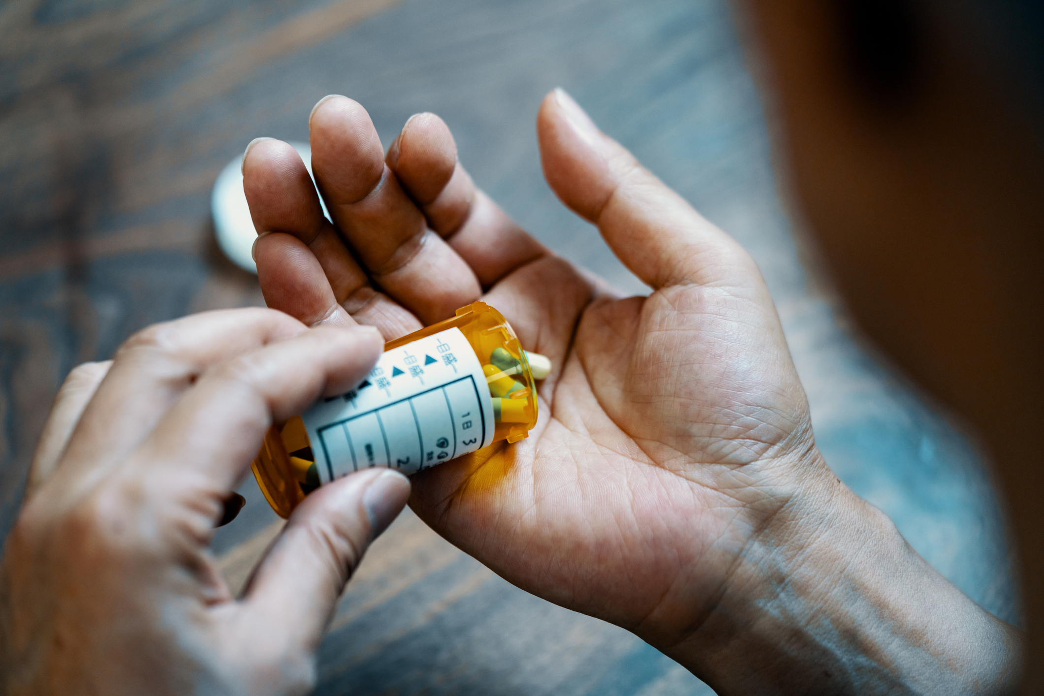 A person is pouring pills from a prescription bottle into their hand.